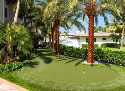 A custom backyard golf green with realistic contours, a sand bunker, and a chipping area in a manicured yard