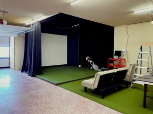 A high-end residential garage completely converted into a luxury indoor golf simulator studio in Clearwater, Florida, featuring a custom impact screen enclosure, seamless edge-to-edge artificial turf flooring, and hidden wiring.