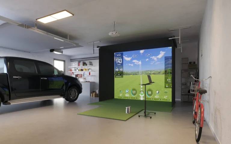 A high-end garage golf simulator in Clearwater, FL, featuring a SkyTrak launch monitor on a green hitting mat. The room features a polished grey epoxy floor, a wall-mounted computer on the right, and a black truck parked to the left. The simulator screen shows a bright, daytime golf course view with a realistic 15% light washout for an authentic indoor-outdoor feel.
