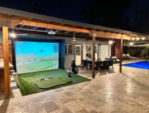 A custom-engineered luxury outdoor golf simulator enclosure installed directly on a residential pool patio in Tampa, Florida, featuring a premium impact screen and artificial turf hitting area situated seamlessly next to the swimming pool.