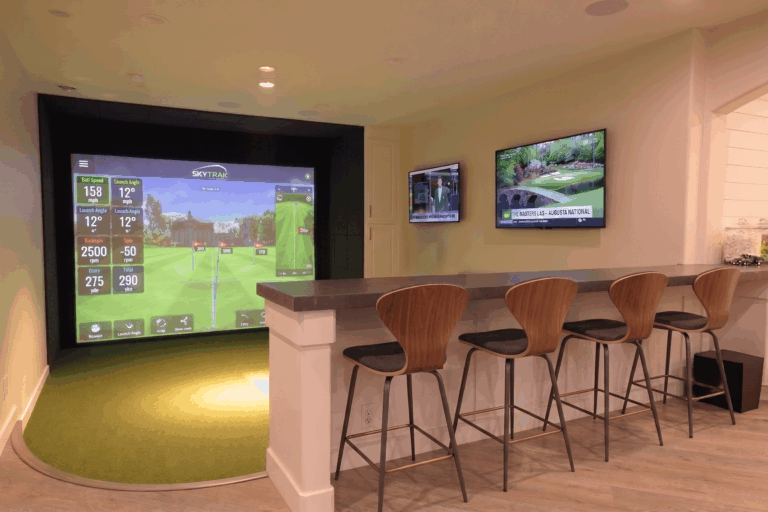 Custom indoor residential golf simulator room in St. Petersburg, Florida, featuring a SkyTrak projection screen, modern curved wood barstools, a built-in bar, and integrated recessed lighting.