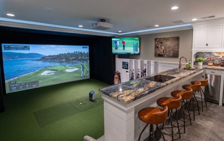 A luxury residential indoor golf simulator in Clearwater, Florida, featuring a custom white entertainment bar with high-end exotic granite countertops and tan leather bar stools overlooking the hitting area.