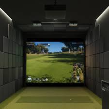 Indoor golf simulator setup: large screen displaying a sunny golf course, with a hitting mat in the foreground.
