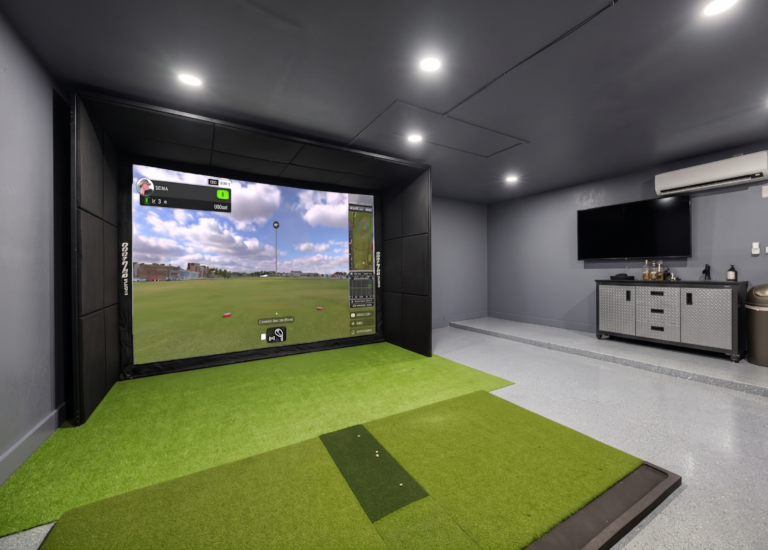 A professional indoor golf simulator room in St. Petersburg, Florida, featuring matte grey walls, industrial diamond plate cabinets, and a premium hitting mat with an overhead can lighting system.