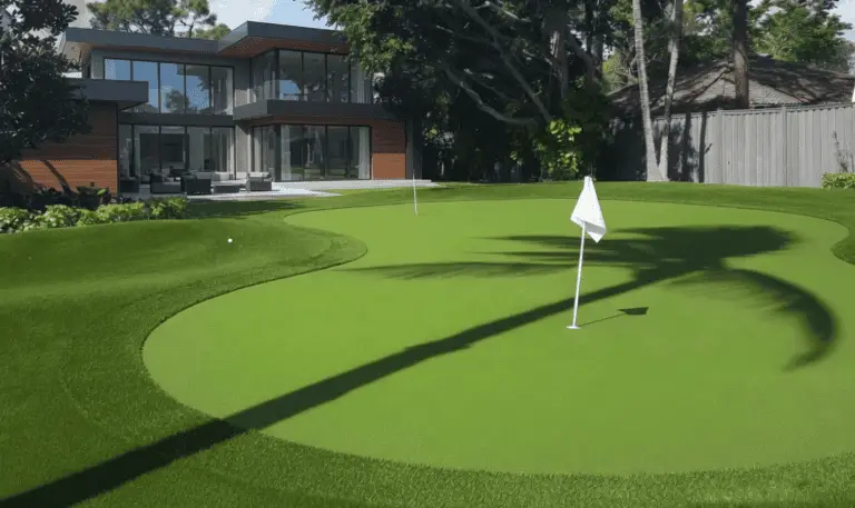 Custom artificial turf putting green with a red flagstick in a modern Belleair, Florida backyard featuring a luxury swimming pool and outdoor pavilion.