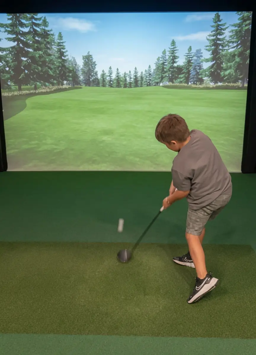 A young boy practicing his golf swing on a home golf simulator in Clearwater, FL, featuring a realistic digital driving range projection screen and custom hitting turf.