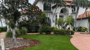 White Mediterranean-style house with an arched entrance and pillars, surrounded by palms and a manicured lawn.