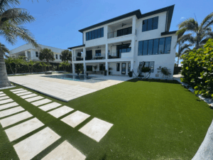 Modern white villa with large glass windows, outdoor pool, and palm trees in a sunny yard.