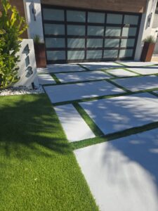 Modern house entrance with frosted glass garage door and geometric concrete stepping stones separated by grass strips.